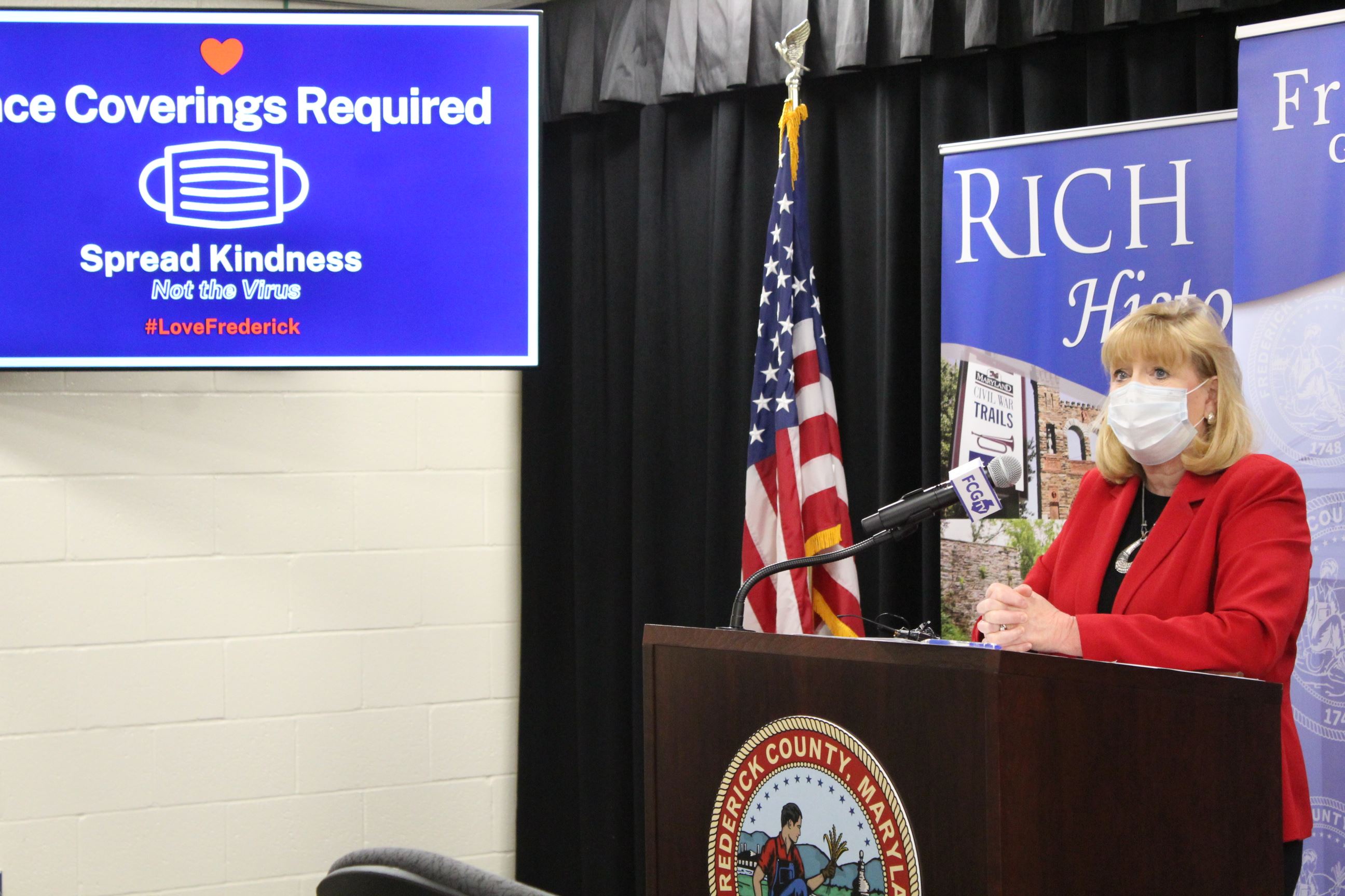 County Executive Gardner Stands at Lectern. Beside her is a sign reading 