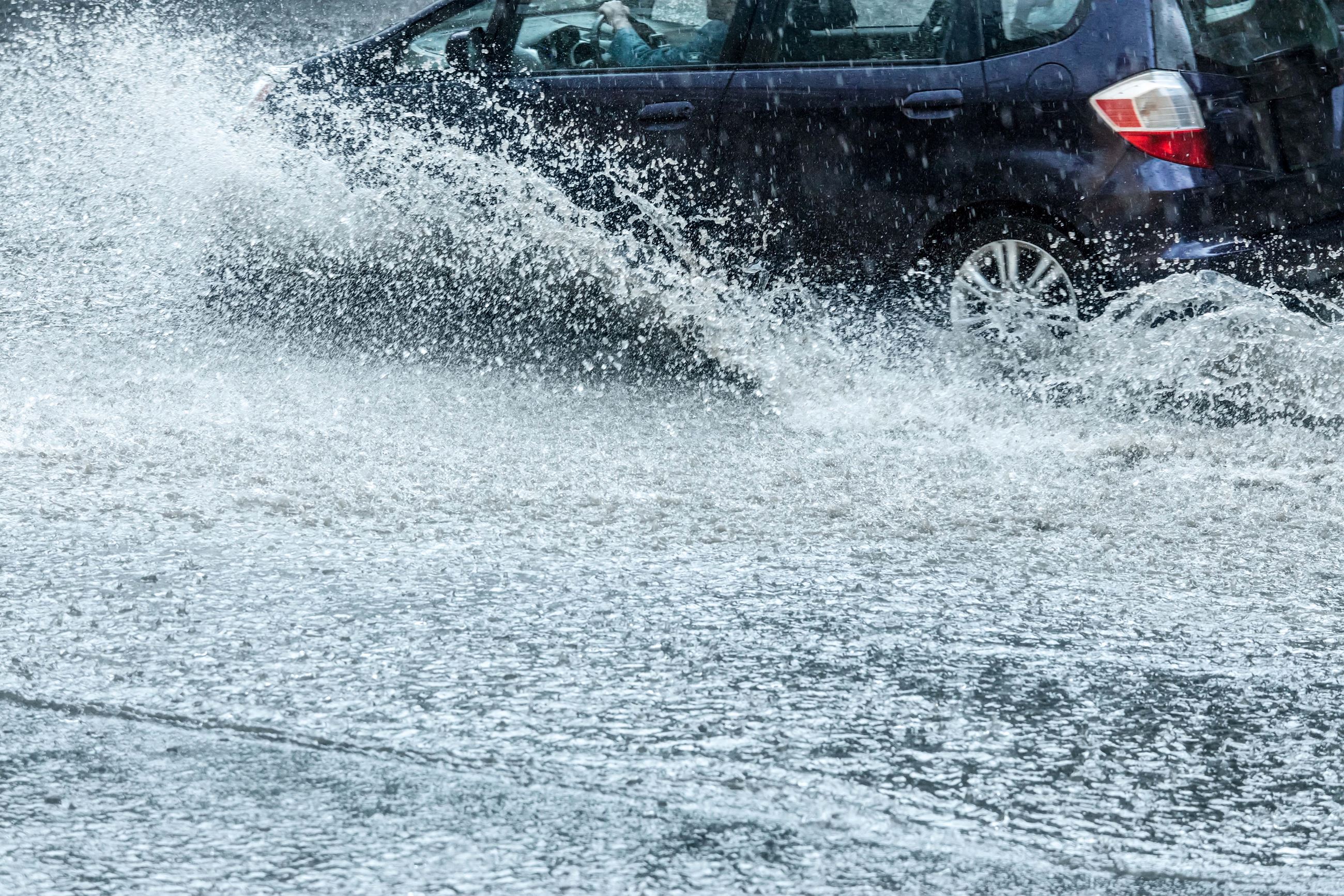 Image shows car driving through a flooded street