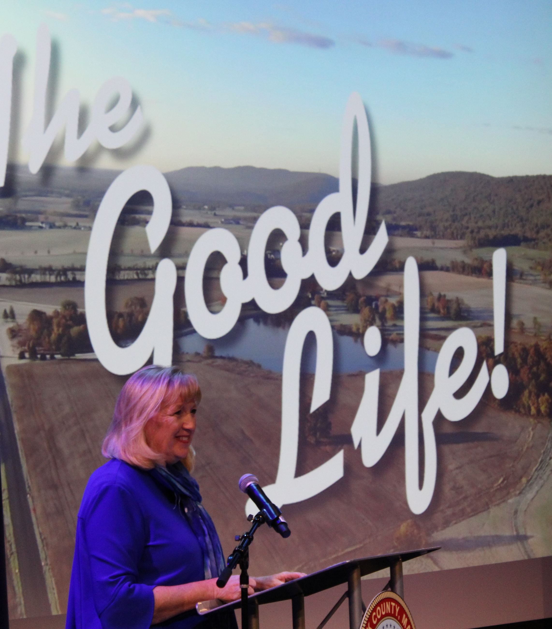 County Executive Gardner stands at a lectern. Behind her is a screen with the words 