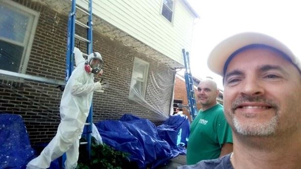 Three people work on the outside of a house.