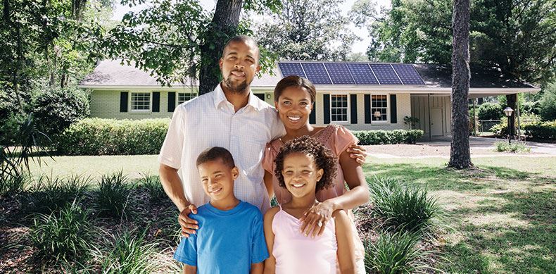Smiling family stands in front of home with solar panels on the roof.