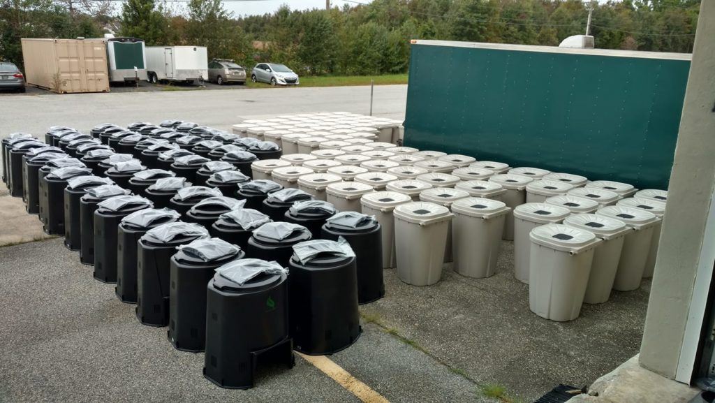 Compost bins and rain barrels lined up for sale.