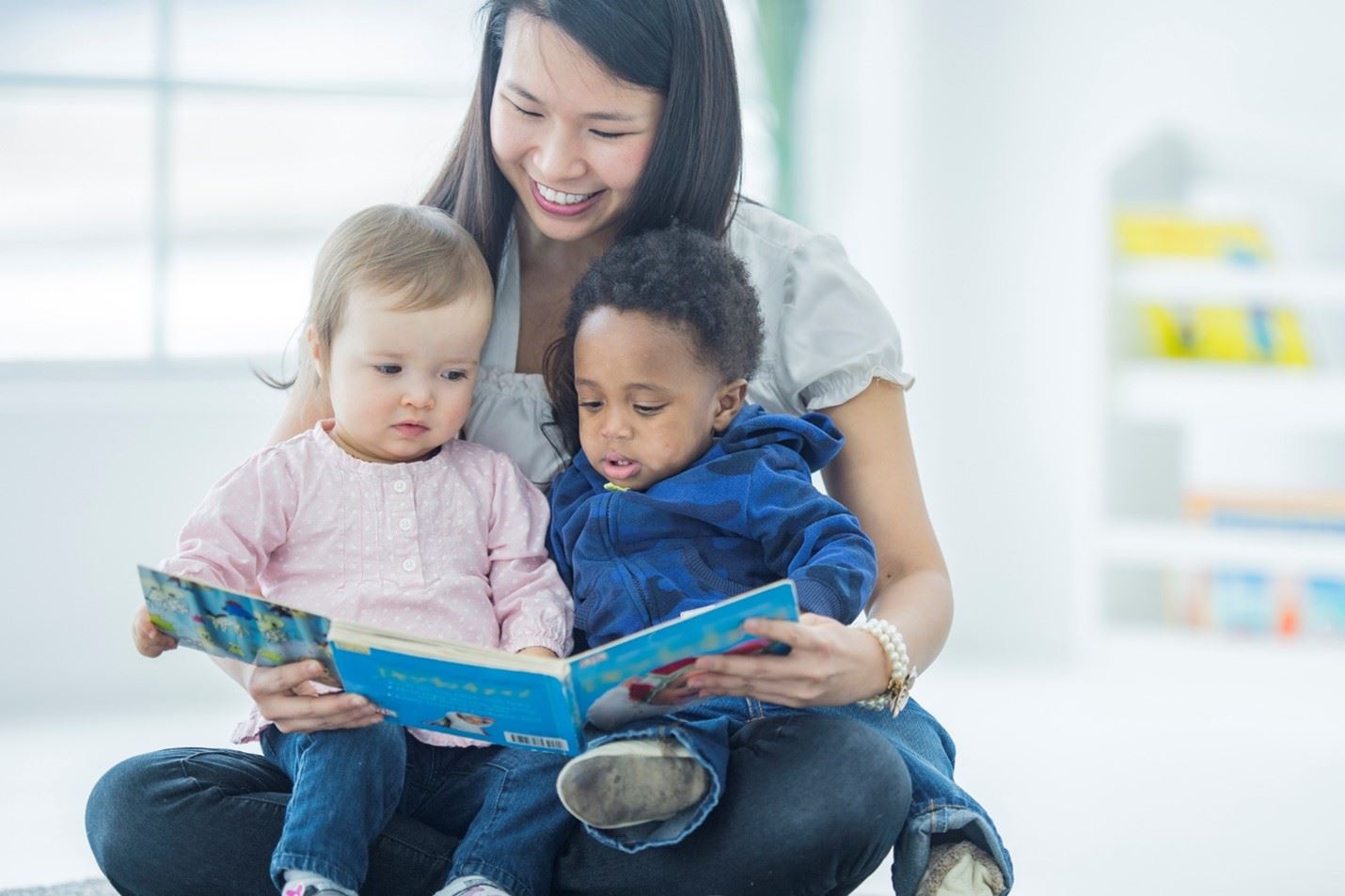 A woman holding two children and reading a book. 
