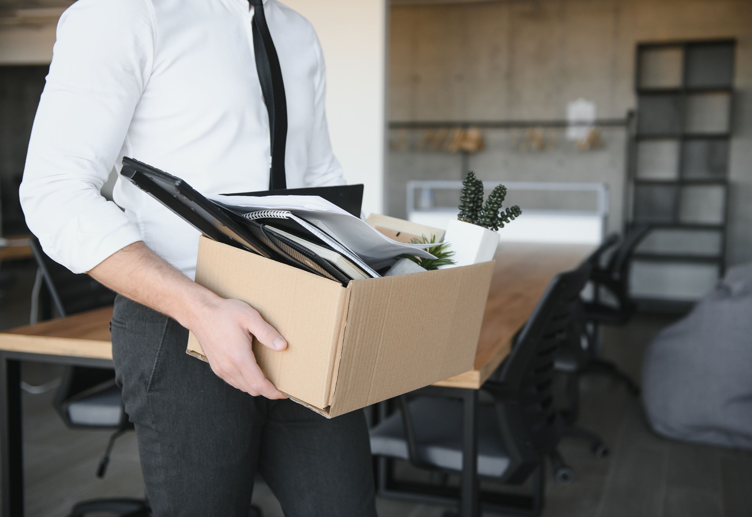 A person carries a box of items away from a desk