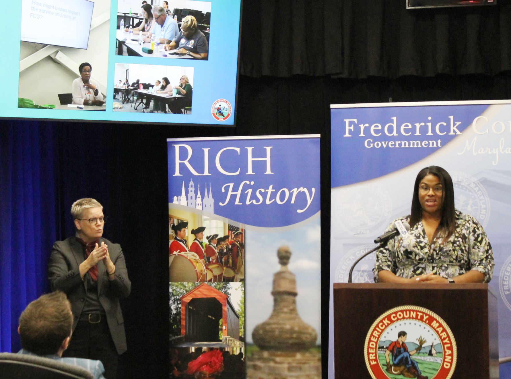 A woman speaking at a lectern. A sign language interpreter looks on.