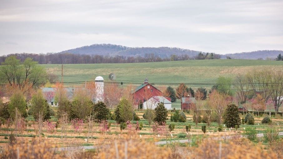 a farm, a field, trees, and hills in the background