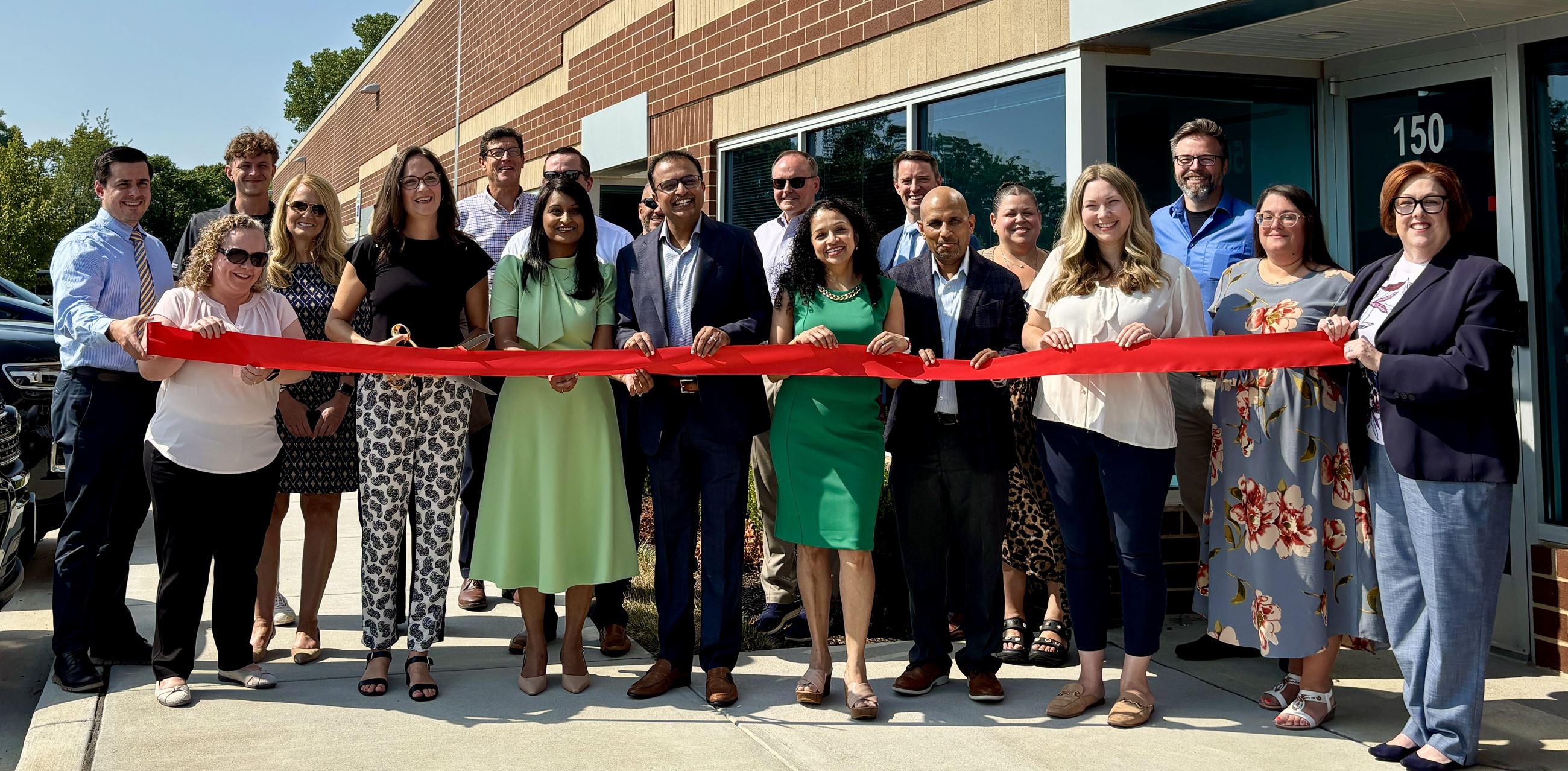 a group of people standing outside behind a red ribbon at a grand opening cermony