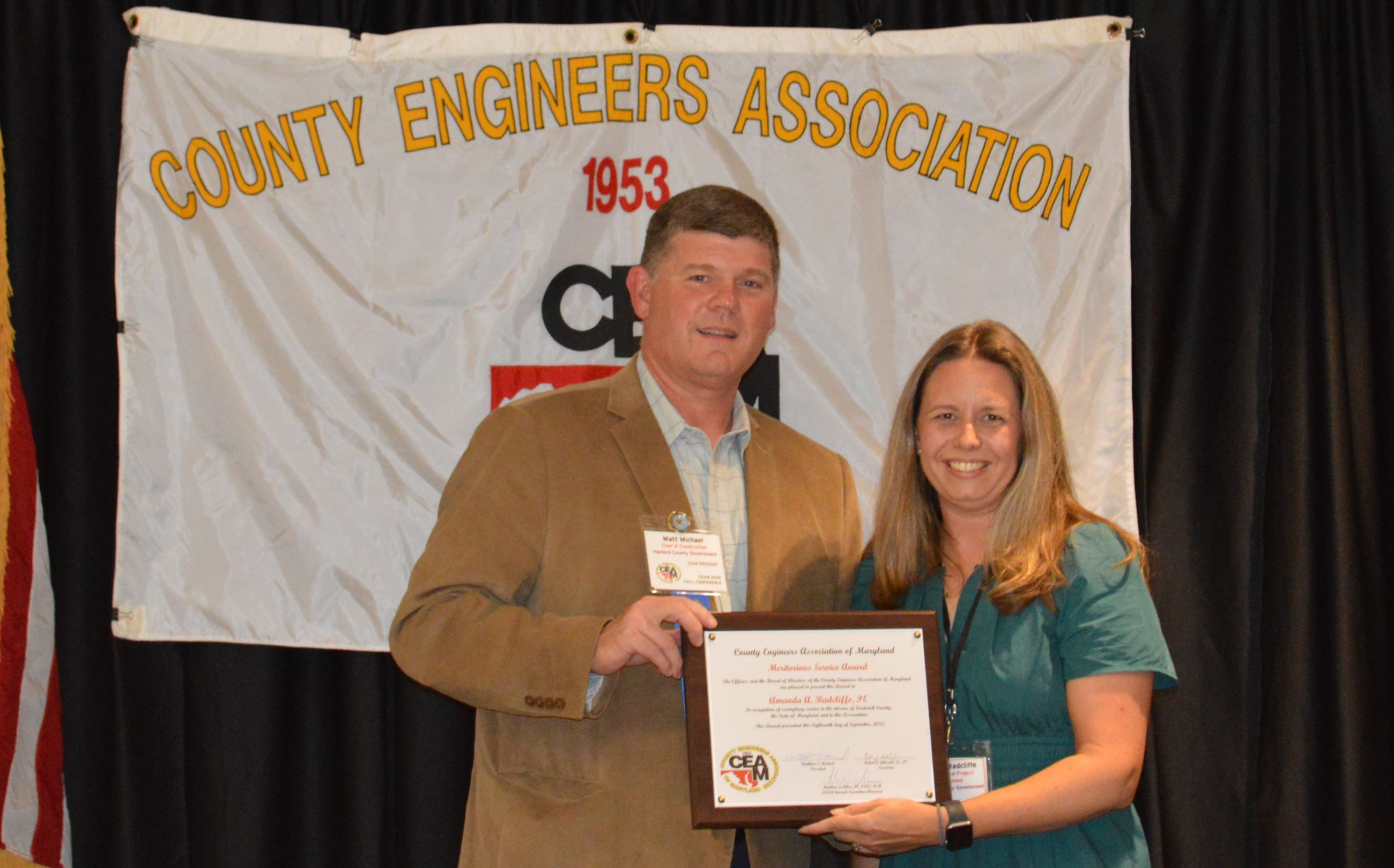Two people posing with an award in front of a banner that says County Engineers Association.