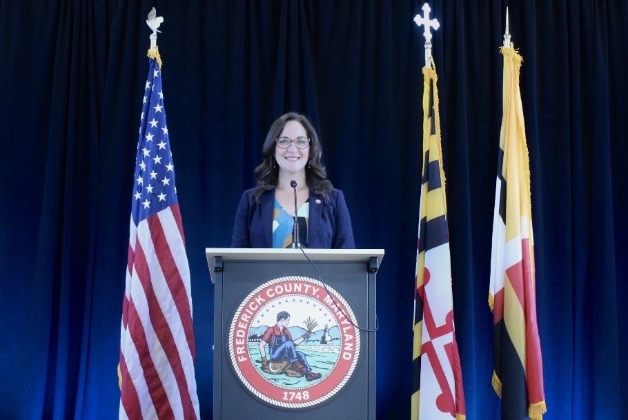 A person standing behind a podium with flags in the background. 